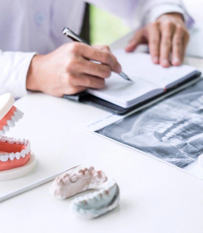 Dentist reviewing dental models and X-rays while taking notes at professional workspace.