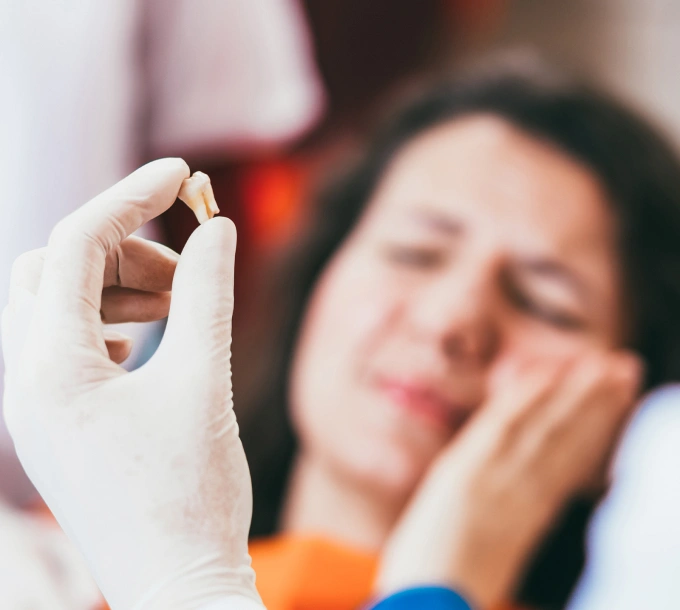 Gloved hand holding dental implant with blurred patient in background at dental office