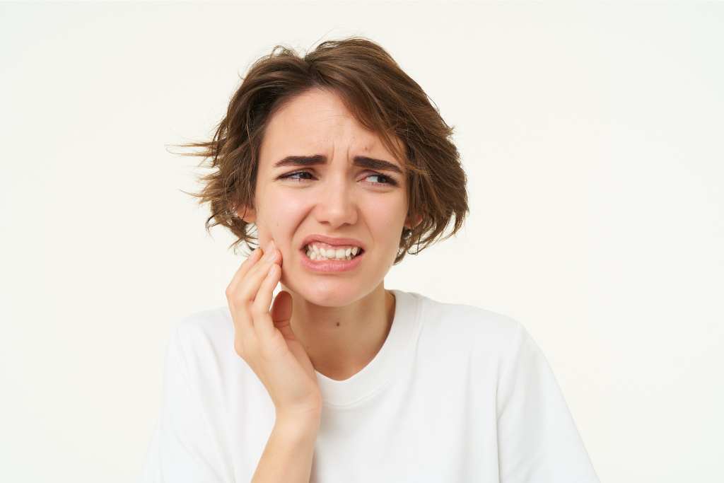 Woman holding her cheek in pain, expressing discomfort from a problematic tooth.